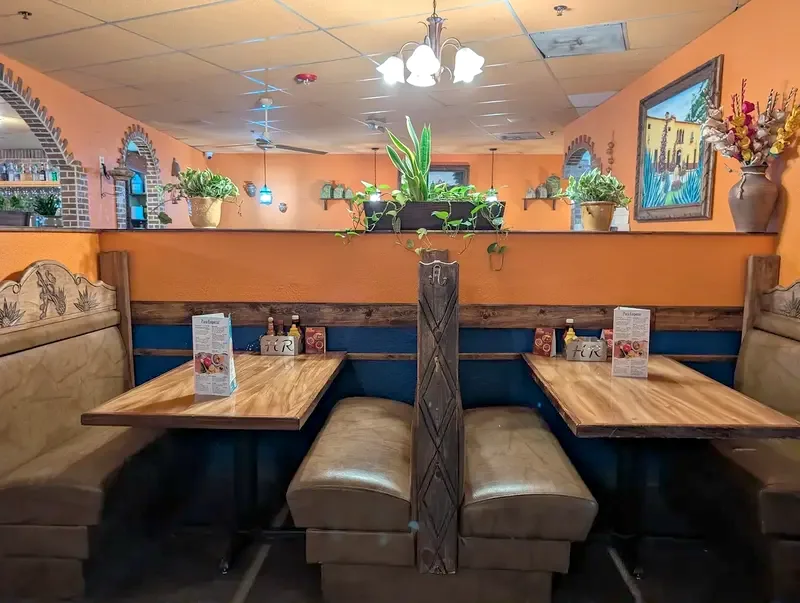 Two wood-top tables with carved, leather-cushioned booths under a framed painting